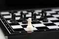 chess piece white pawn stands on edge of chessboard against background of group of black pieces