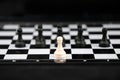 chess piece white pawn stands on edge of chessboard against background of group of black pieces