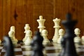 Chess pieces arranged on chessboard in shot at shoulder level or at eye level focus on background with wooden wall behind moody Royalty Free Stock Photo