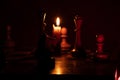 Chess pieces stand on a chessboard and next to a burning candle in the dark, playing Royalty Free Stock Photo