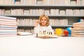 Chess school. Concentrated kid play chess. Smart child play chess in the library by the bookshelves. Educational concept Royalty Free Stock Photo