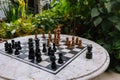 Chess wooden pieces on board in patio with green plants. Chess table in garden. Outdoor stone chessboard with figures. Royalty Free Stock Photo