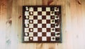 A chessboard made of wood with chess pieces placed on it stands on a table