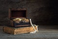 Chest with gold coins on an old book on a wooden table, vintage style, concept of wealth, pirate treasure, greed
