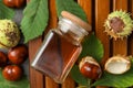 Chestnuts, leaves and jar of essential oil on wooden table, flat lay