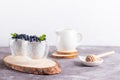 Chia pudding with blueberries in glasses on a wooden stand with a honey stick and cream jug on a light background