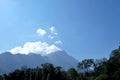 Blurred white fluffy clouds blue sky in bright day over high mountain with a line of tropocal trees growing