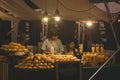 Chiang Mai, Thailand - November 2017: Woman selling mango sticky rice behind stand with pile of mangoes in night market