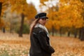 Chic beautiful trendy young woman in a stylish black hat in a brown vintage jacket walks in the autumn park. European girl in the Royalty Free Stock Photo