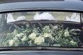 A chic bouquet of white roses behind the glass of the back seat of a wedding car