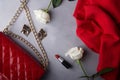 Chic fashion accessories with red purse and classic beauty products among roses