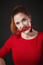 A chic red-haired young woman in a red overalls holds a hot chili pepper in her hands Royalty Free Stock Photo