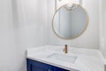 Half bathroom with a blue cabinet and gold mirror.