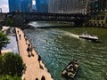 Chicago River during a colorful summer, people on riverwalk, man fishes out of parked fishing boat, kayakers and speedboat pass