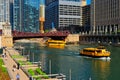 Chicago River recreation and utilization with water taxis, and commuters walking on the riverwalk on colorful spring morning.