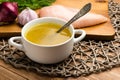 Chicken bouillon in the white bowl on the rustic wooden background.