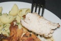 Chicken breast fried with spices, boiled pasta with herbs, a metal fork with a cut piece of breast on a white plate Royalty Free Stock Photo