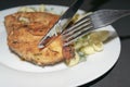 Chicken breast fried with spices, boiled pasta with herbs, metal fork and knife which cut a piece of the breast on a