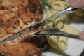 Chicken breast fried with spices, boiled pasta with herbs, metal fork and knife which cut a piece of the breast on a