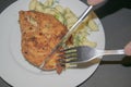 Chicken breast fried with spices, boiled pasta with herbs, metal fork and knife which cut a piece of the breast on a white plate