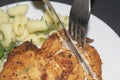 Chicken breast fried with spices, boiled pasta with herbs, metal fork and knife which cut a piece of the breast on a white plate Royalty Free Stock Photo