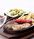 Chicken breast steak, beef steak, fried sausages, french fries, served on a hot plate, with pickles and barbecue sauce Royalty Free Stock Photo