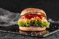 Chicken burger with tomatoes, lettuce and sauce on slate black background, close up