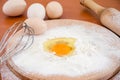 Chicken eggs, flour, whisk and rocking chair on the table. The process of making dough. Close-up. Broken egg in flour on a wooden Royalty Free Stock Photo