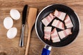 Chicken eggs, knife, spatula, frying pan with slices of smoked brisket on table. Top view