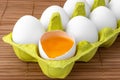 Chicken eggs in a package, isolated on a wooden table, one egg is open Royalty Free Stock Photo