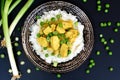 Chicken fillet with curry, green peas, spring onion and on dark plate on black background