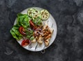 Chicken kebab, grilled zucchini, tomatoes, lettuce, red onion salad on a dark background, top view Royalty Free Stock Photo