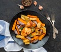 Chicken legs and thighs baked with sweet potatoes or carrots, white and purple onions, regular potatoes on a black ceramic plate Royalty Free Stock Photo