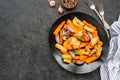 Chicken legs and thighs baked with sweet potatoes or carrots, white and purple onions, regular potatoes on a black ceramic plate Royalty Free Stock Photo