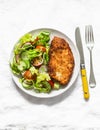 Chicken milanese and fresh romaine salad, cherry tomatoes, radishes, cucumbers salad - delicious lunch on a light background, top