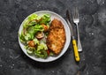 Chicken milanese and fresh romaine salad, cherry tomatoes, radishes, cucumbers salad - delicious lunch on a dark background, top