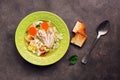 Chicken noodle soup, potatoes, carrots in a green plate served with fried toasts on a dark rustic background. Top view, copy space