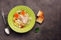 Chicken noodle soup, potatoes, carrots in a green plate served with fried toasts on a dark rustic background. Top view, copy space