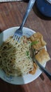 chicken noodles with a bit of mustard greens and wonton crackers in a white bowl