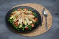 Chicken salad with avocado, rucola and cherry tomatoes in a black plate on gray stone background. Royalty Free Stock Photo