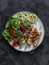 Chicken skewers, grilled zucchini, tomatoes, lettuce, red onion salad on a dark background, top view Royalty Free Stock Photo