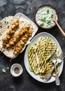 Chicken skewers, grilled zucchini, tortillas and tzadziki sauce - delicious greek style lunch on a dark background, top view