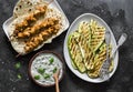 Chicken skewers, grilled zucchini, tortillas and tzadziki sauce - delicious greek style lunch on a dark background, top view