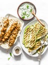 Chicken skewers, grilled zucchini, tortillas and tzadziki sauce - delicious greek style lunch on a light background, top view