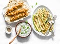 Chicken skewers, grilled zucchini, tortillas and tzadziki sauce - delicious greek style lunch on a light background, top view