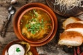 Chicken soup or broth with noodles, herbs and vegetables in bowl with sour cream, bread, pepper on wooden rustic background.