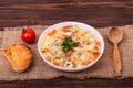 Chicken soup with vegetables and noodles on a textured burlap with slices of toast, a wooden spoon and a cherry tomatoe