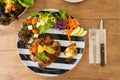 Chicken steak serve with mashed potato and salad on a black and white plate on a wooden table