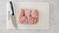 Chicken thighs in plastic container, and kitchen knife close-up on a white plastic cutting board on a kitchen table Royalty Free Stock Photo