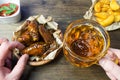 Chicken wings in a fragrant and pungent sauce with sesame seeds. A glass of fresh cold beer and fried potatoes with rustic tomato Royalty Free Stock Photo